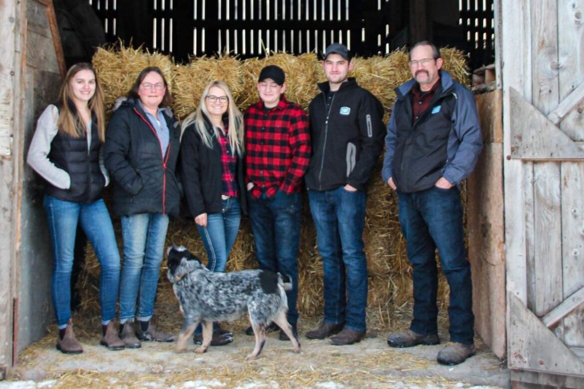 The Haanover View Farm Family and dog standing in front of an open barn door with straw bales in the background.